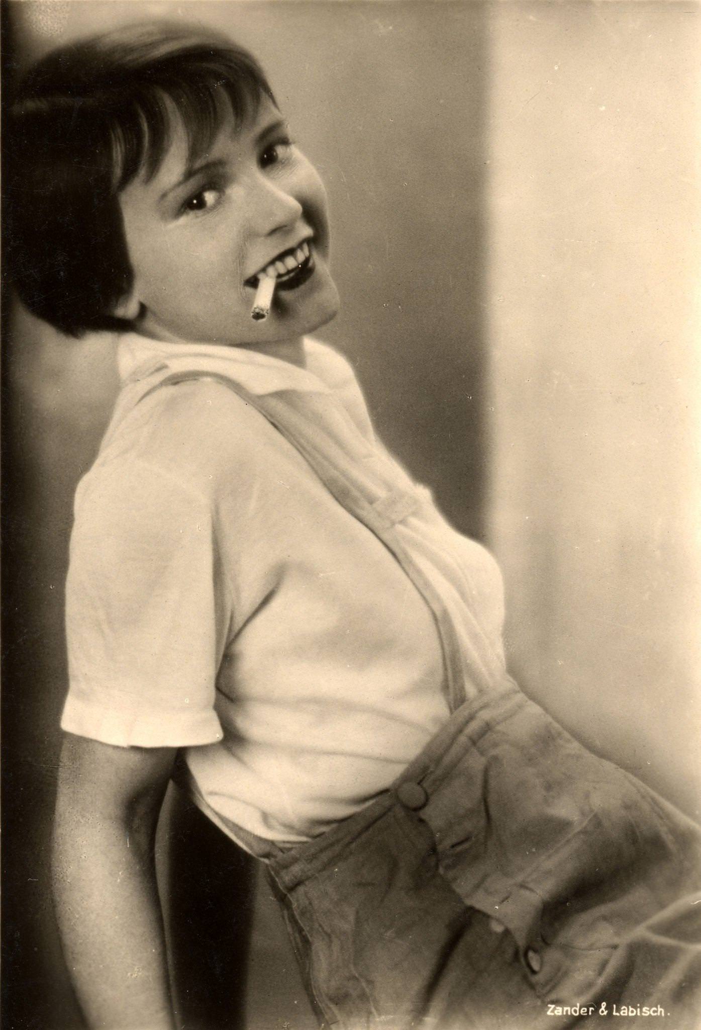 American actress Louise Brooks poses in lederhosen and smokes a cigarette in this postcard image from Germany, 1920s or 1930s.