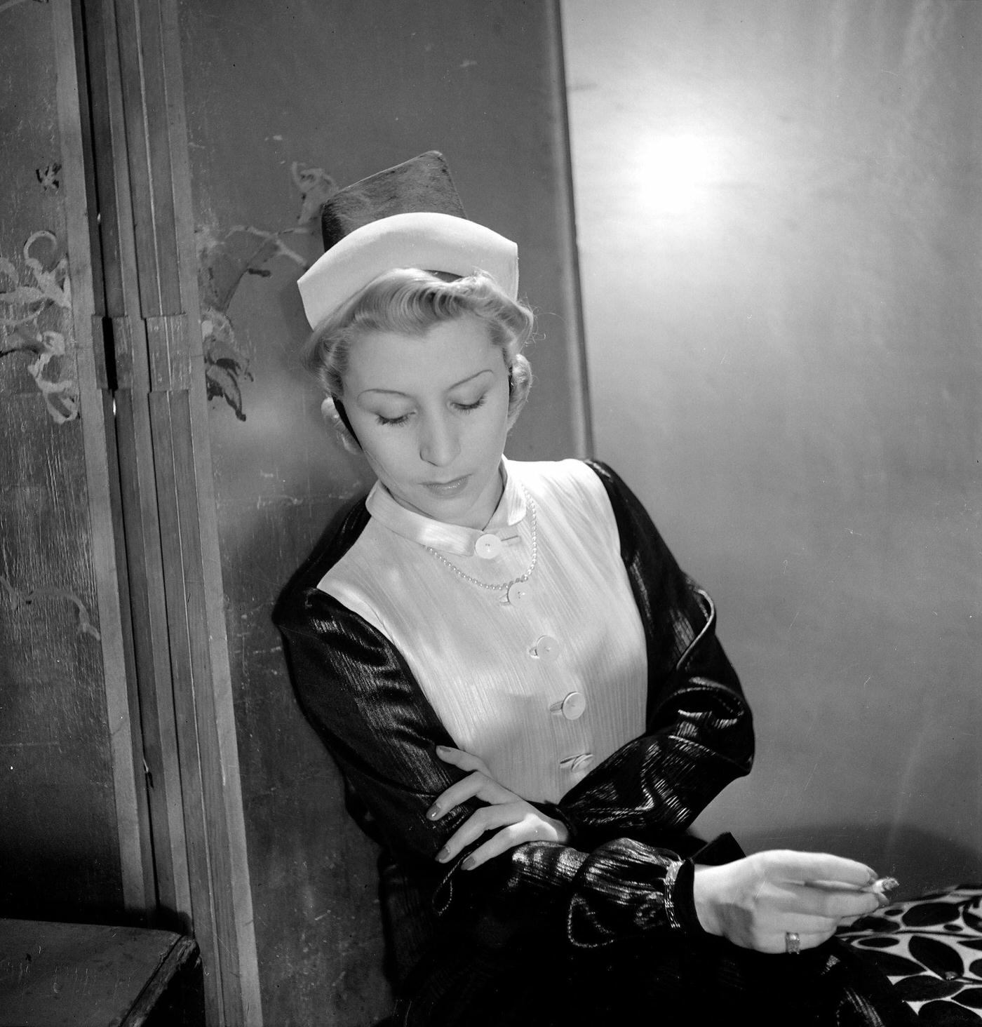 A fashion model sits and smokes a cigarette wearing a hat designed by French fashion designer Jeanne Lanvin, Paris, 1935.