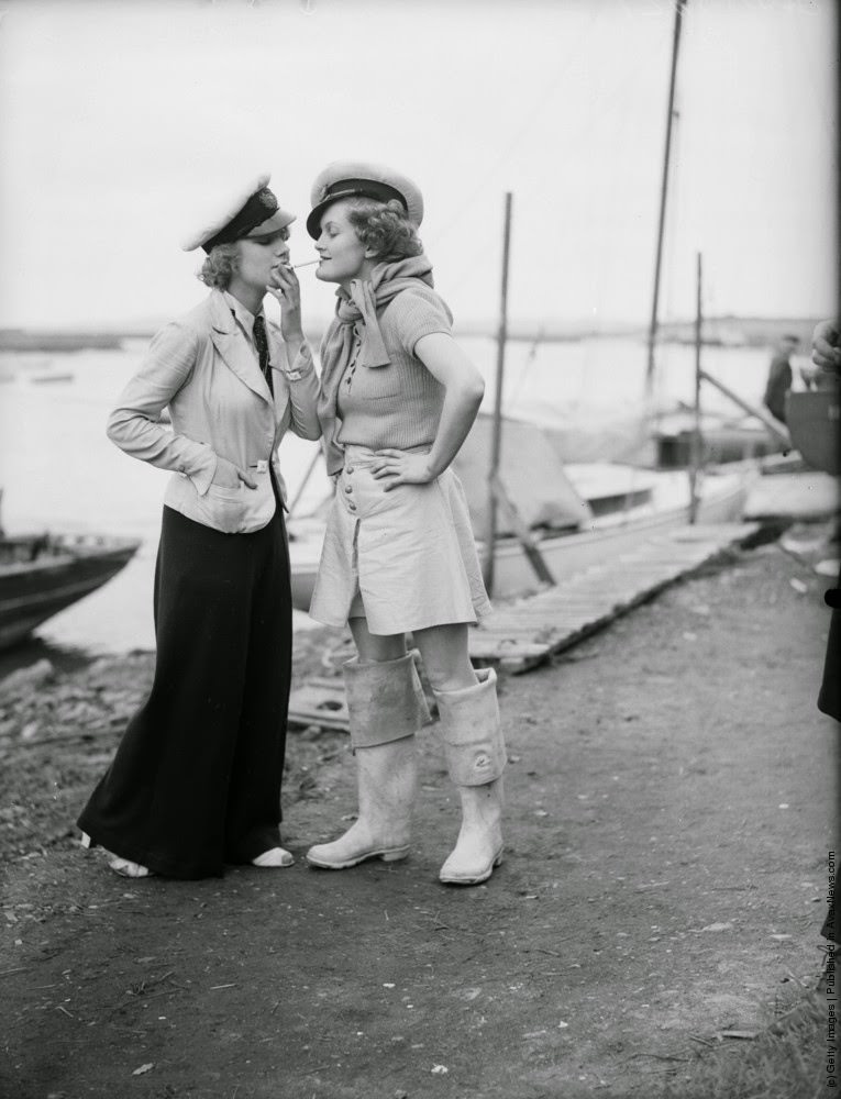 Two women in yachting caps. One is lighting her cigarette from the others, 9th May 1936