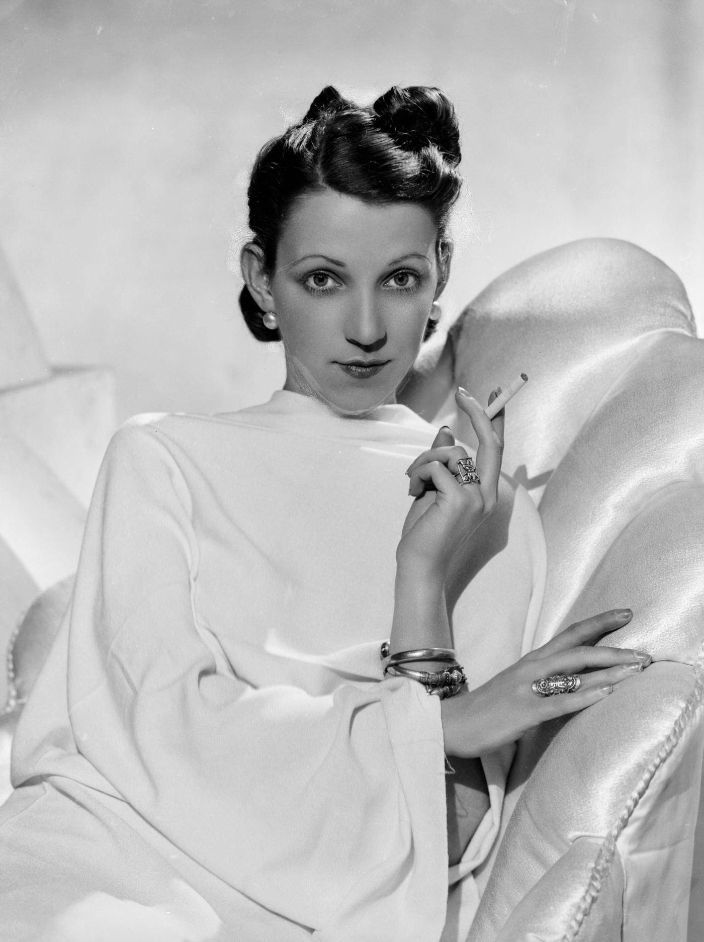 A glamorous fashion model wearing a vestal gown and resting on a sumptuous recliner, 1935