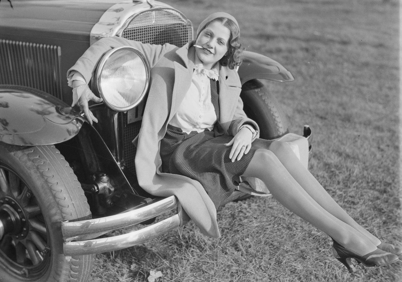 Young woman sitting on the bumper of a car, smoking a cigarette, 1930