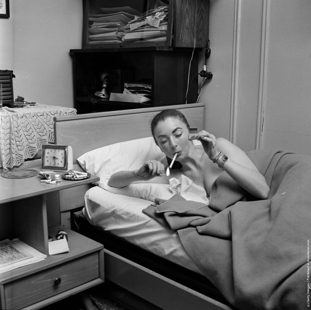 A member of a teenage girl gang lying in bed smoking a cigarette, circa 1955.