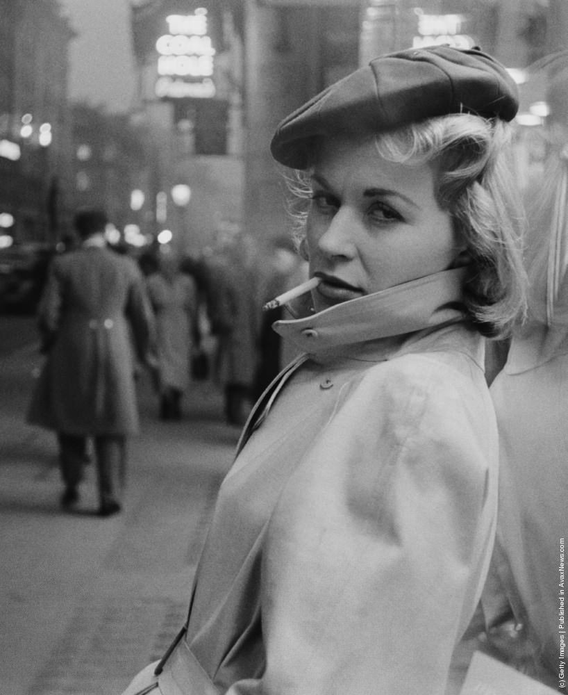 Austrian actress Julia Arnall, leaning against a shop window and smoking a cigarette. 27th February 1956.