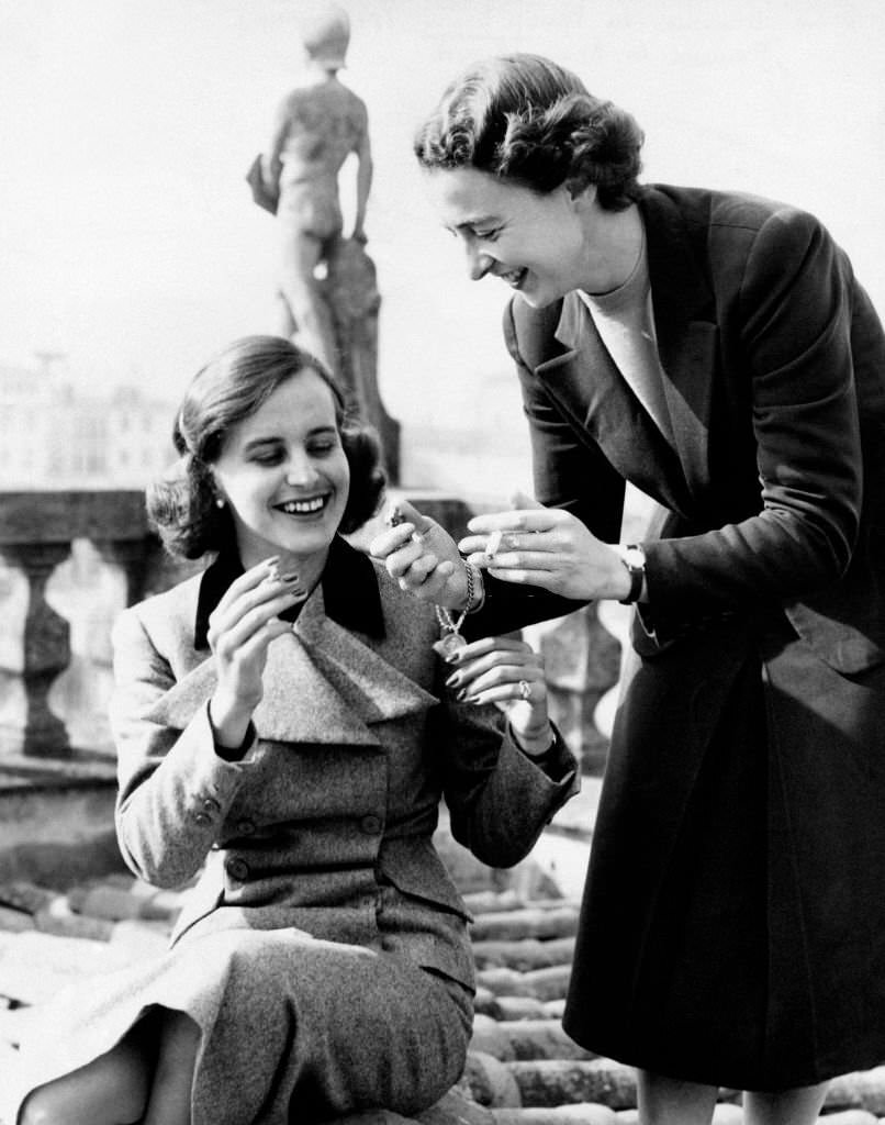 On a terrace, Italian baroness Francesca Ricasoli lighting a cigarette to Italian artist, princess Giuliana Corsini, 1950s.