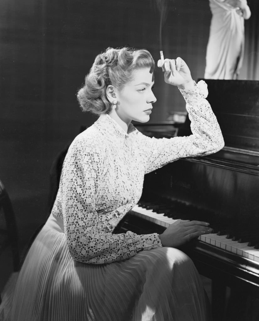 American screen star Lauren Bacall smoking, sits thoughtfully at the piano for the film 'Young Man With A Horn,' 1950.