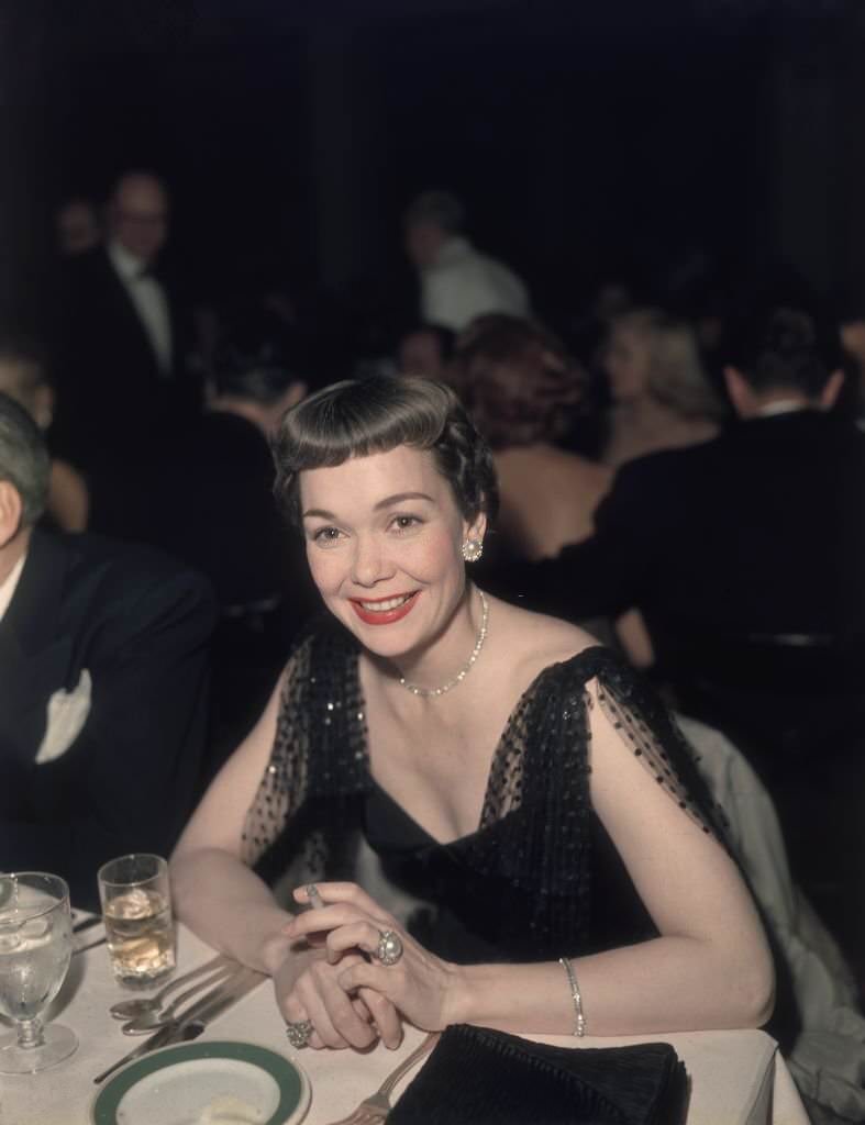 American actor Jane Wyman smoking a cigarette at a formal event, dressed in black, 1950.
