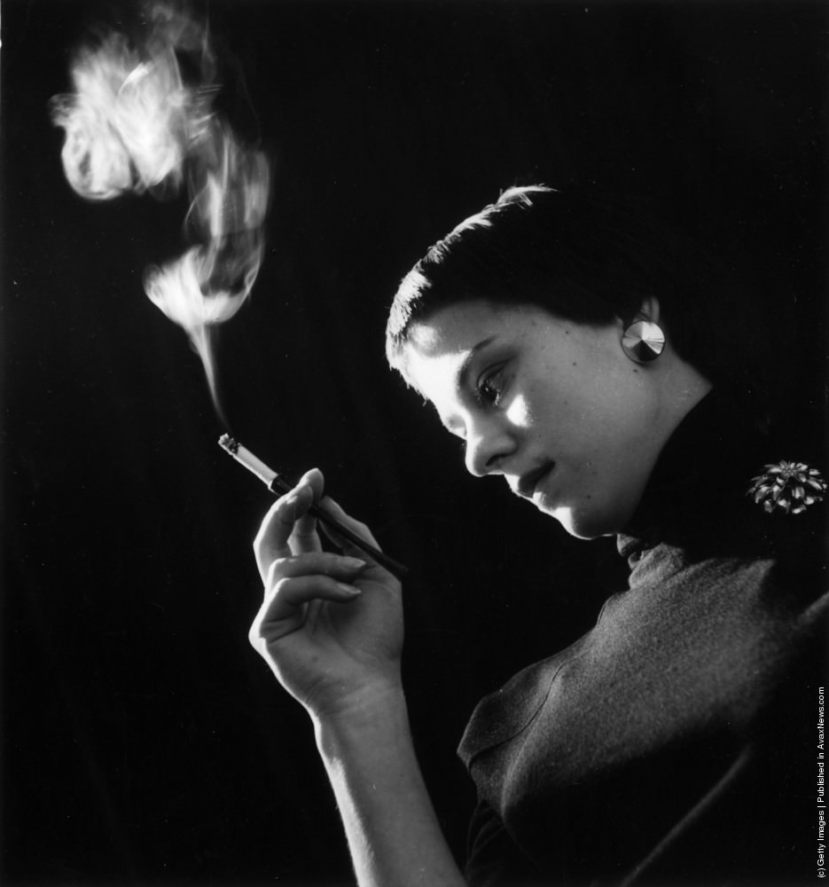 A theatre chorus girl smoking a cigarette in an elegant holder, 1954.