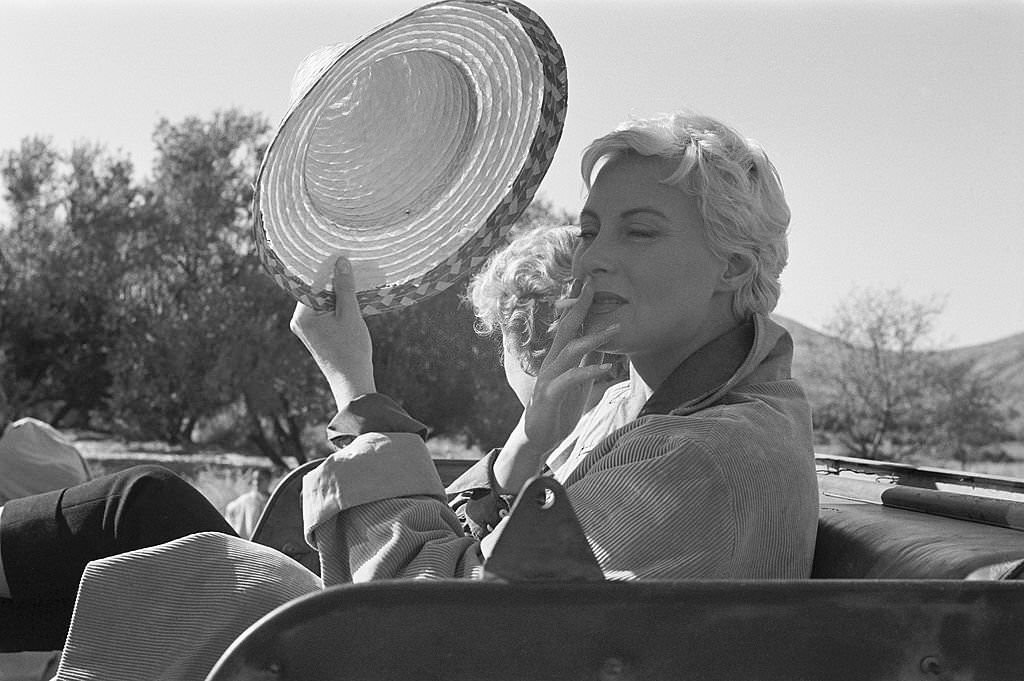Shooting of the film 'Oasis' by Yves Allegret in Morocco: Michèle Morgan smoking a cigarette in a jeep next to Cornell Borchers, 1955.