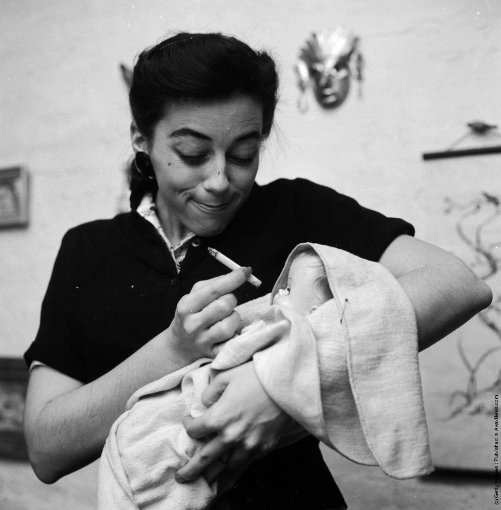 Naturally, it is important that a baby learn the right habits. This woman demonstrates that smoking is wrong for babies, 1955. From a series of images parodying women's lifestyle and beauty magazines.