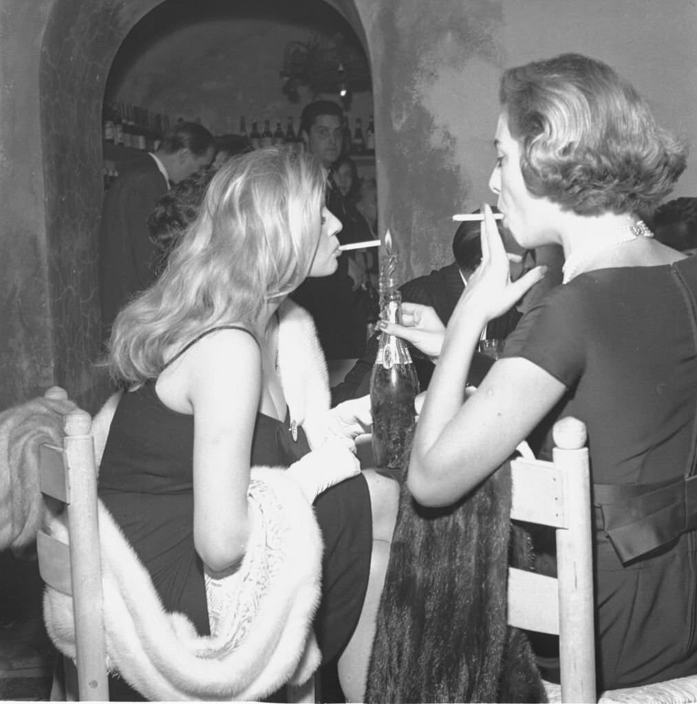 Actress Anita Ekberg smokes a cigarette with Gaea Pallavicini at a dinner party in Rome, 1958.