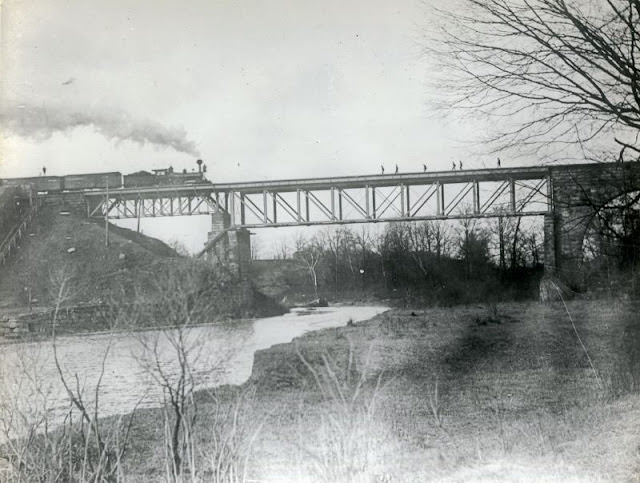 This bridge may be earlier than the Howe Truss steel/iron bridge that collapsed in 1876. Later photos show stone arches on both sides of the bridge