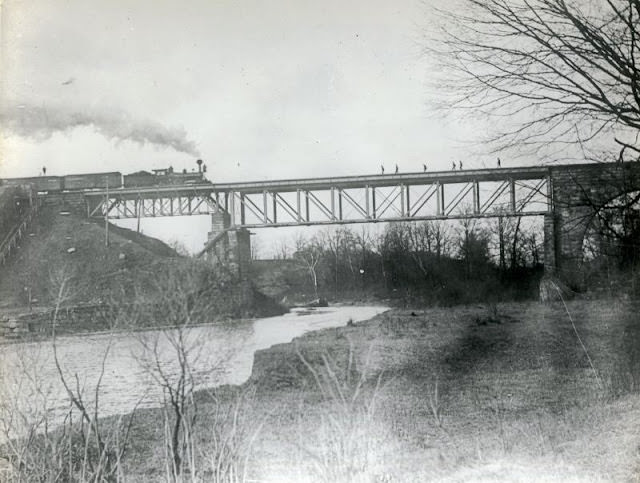 This bridge may be earlier than the Howe Truss steel/iron bridge that collapsed in 1876. Later photos show stone arches on both sides of the bridge