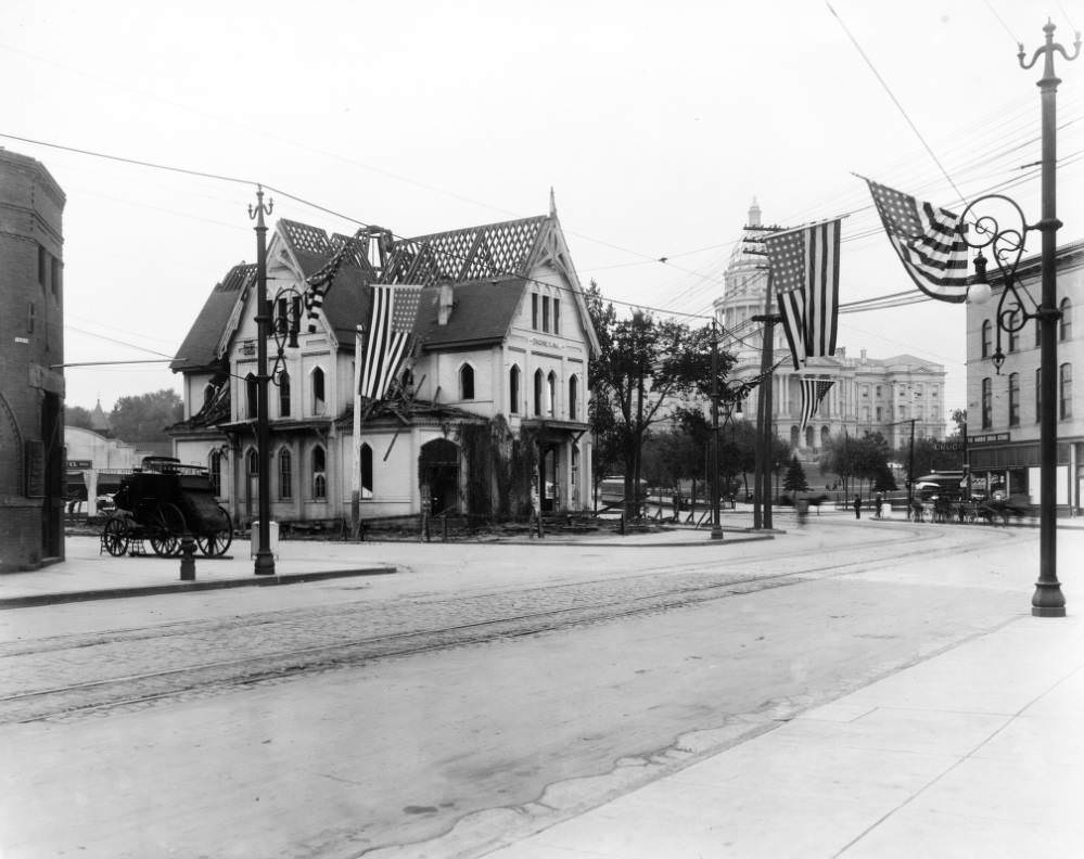 Engine House Number One being dismantled at the corner of Colfax and Broadway, featuring stagecoach and flags, 1909.