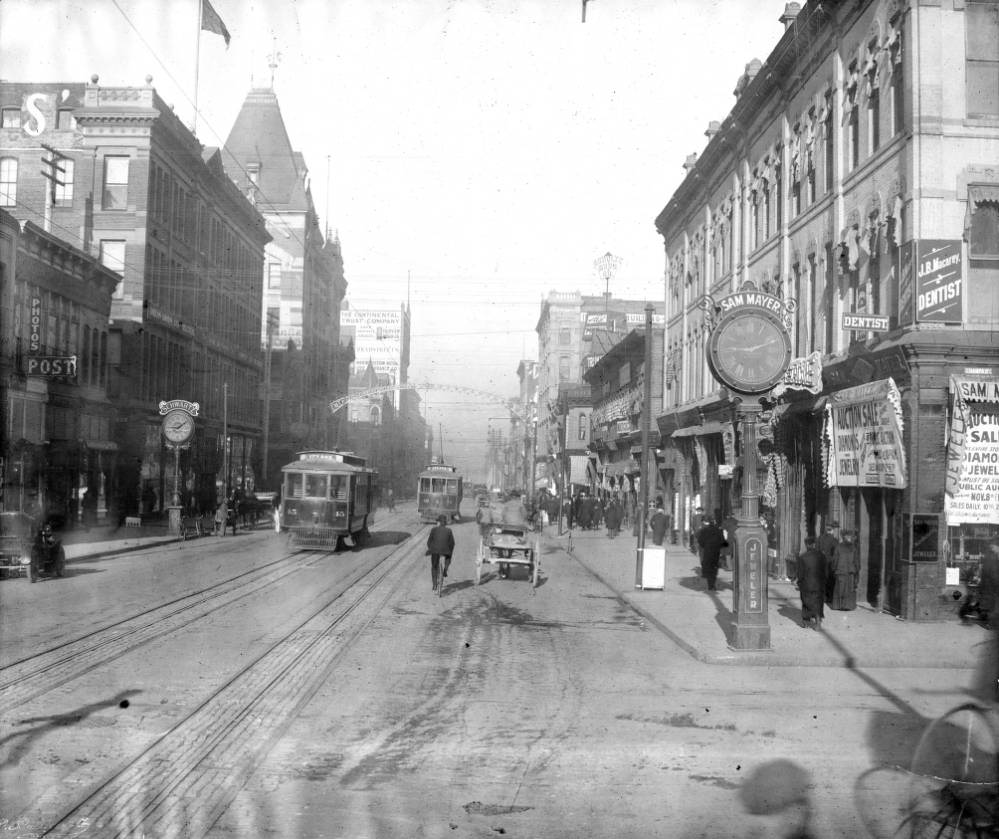 Trolleys number 45 and 42 at 16th and Champa, featuring various business signs and traffic, 1905.