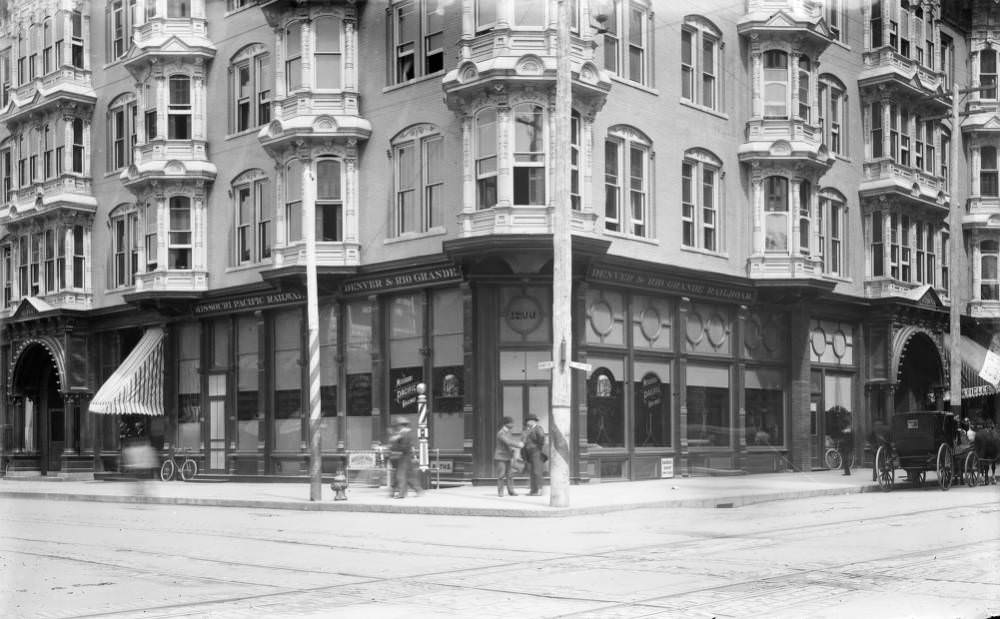 Men shaking hands outside Albany Hotel, featuring railroad signs and a barbershop pole, 1900s