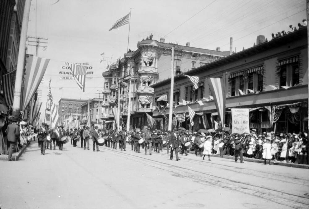 Marching band and spectators during a parade on 17th Street, Denver, featuring a banner for the National Association of Civil War Musicians, 1900s