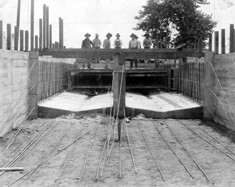 Men pose by concrete forms during flood control construction in Denver, 1900s