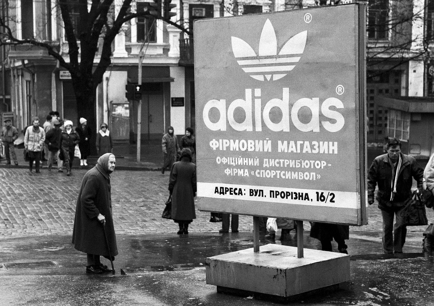 Elderly Woman Stands Near an Adidas Billboard in Kiev