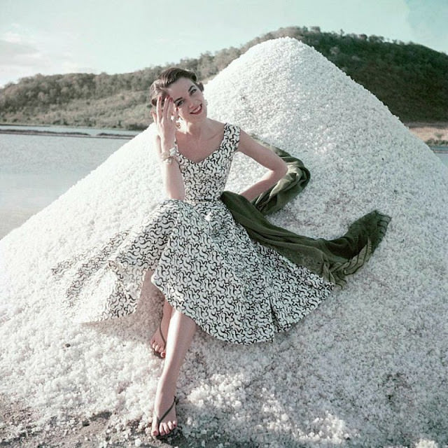 Theo Graham wears a white pique dress embroidered in deep moss green, sitting on salt flats in Cabo Rojo, Puerto Rico, 1954.