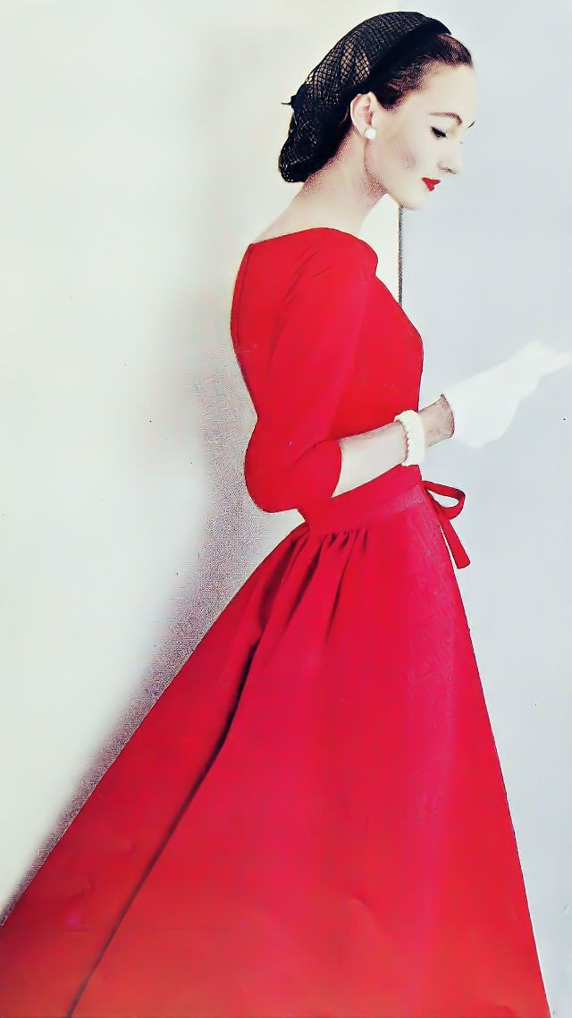 Evelyn Tripp in a red silk faille dress with back fullness, accented with a black snood and jewelry, 1956.