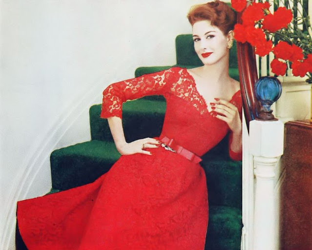 Nancy Berg in a vivid red re-embroidered lace dress with a scalloped neckline, 1957.