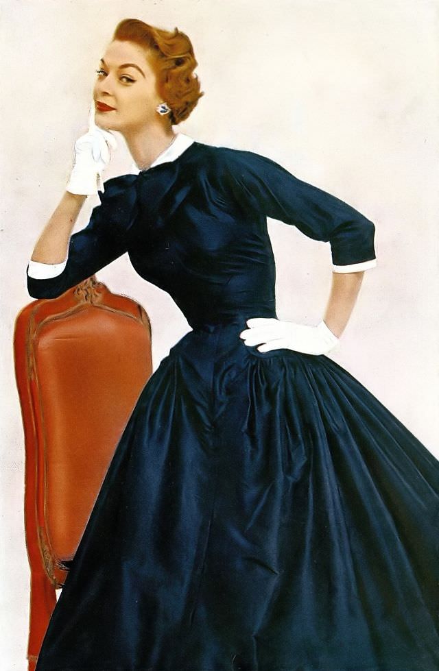 Jean Patchett wears a navy silk taffeta basque dress with a pique collar and cuffs by Jerry Parnis, 1954.