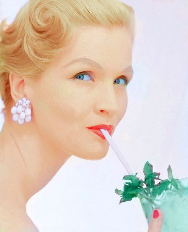 Marjorie Cato sips mint-iced lemonade while wearing chalk-bead earrings by Hattie Carnegie, 1954.