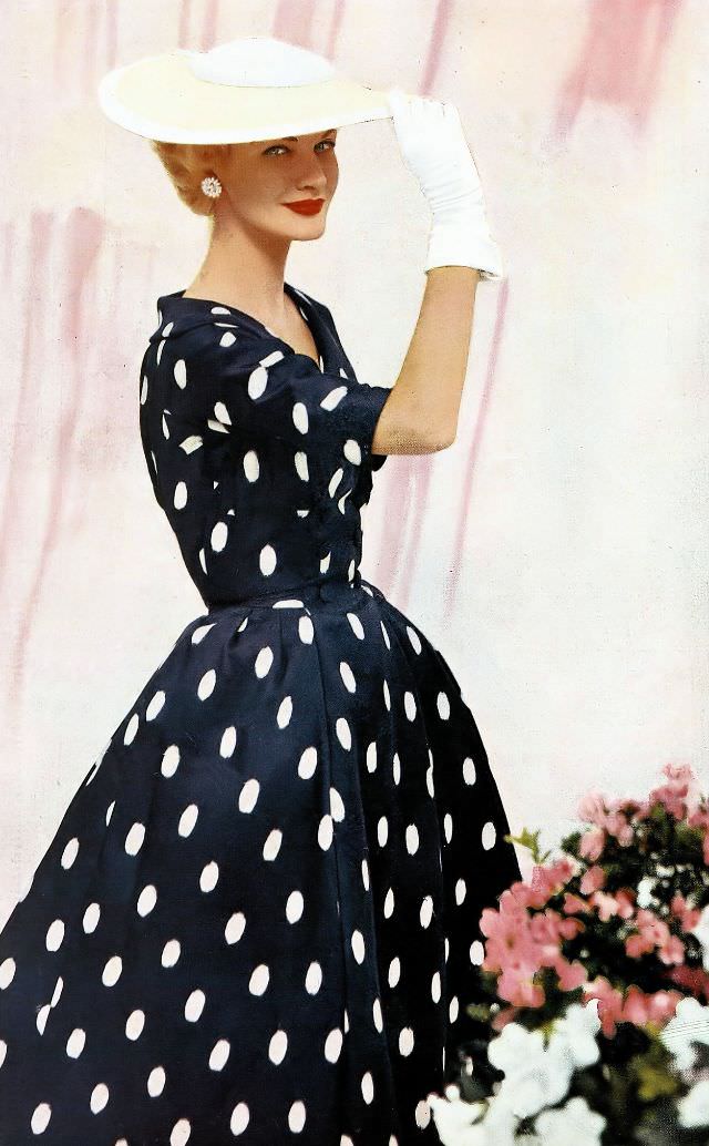 Sunny Harnett in a navy and white saucer-dot silk dress with a bell skirt by Kaspar, and a straw sailor hat by Sally Victor, 1954.
