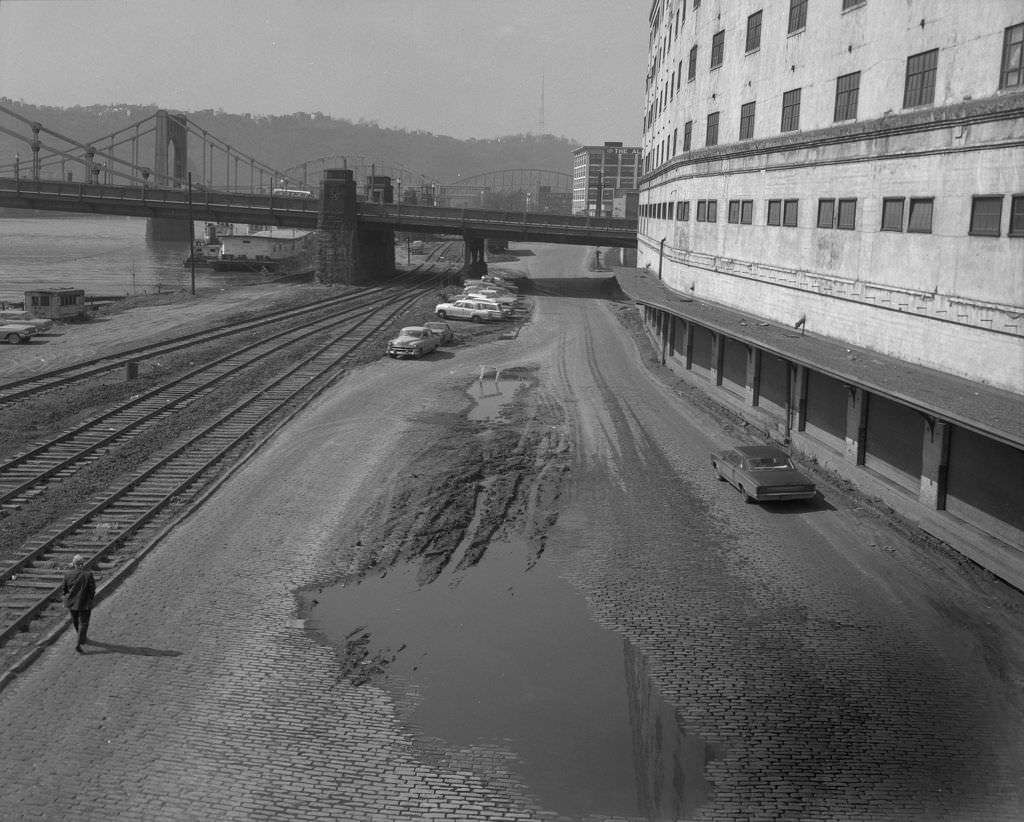 Man walking near train tracks on River Avenue: tugboats and Sixth and Seventh Street Bridges visible, 1966.