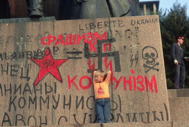 Boy standing on the heavily graffitied base of a statue of Lenin, Ukraine, 1991