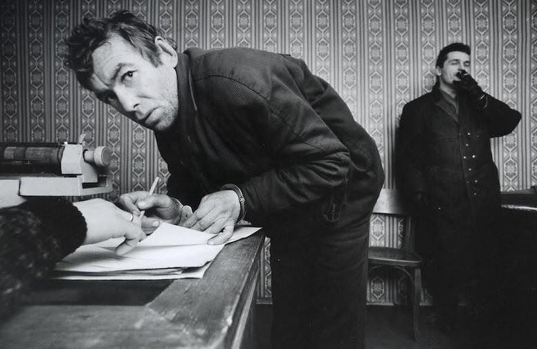 A petty thief signing his confession at the local police station, December 1992. The arresting officer stands in the background.