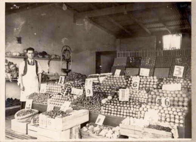 A fruiterer in a white apron in his greengrocer shop