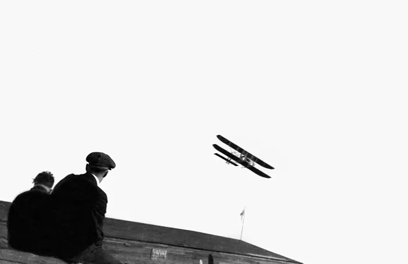 Two men watch an early biplane fly in Ohio, 1910s.
