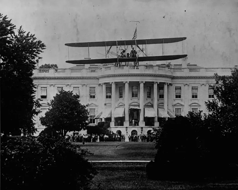 A biplane flying over the White House lawn.