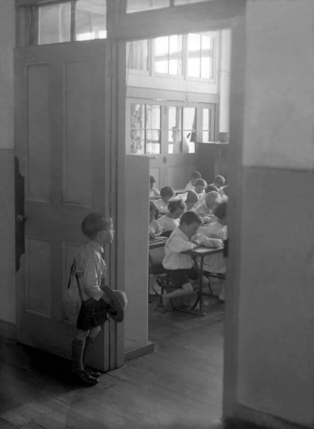 A young Australian boy stares into a classroom already full of students, circa 1930