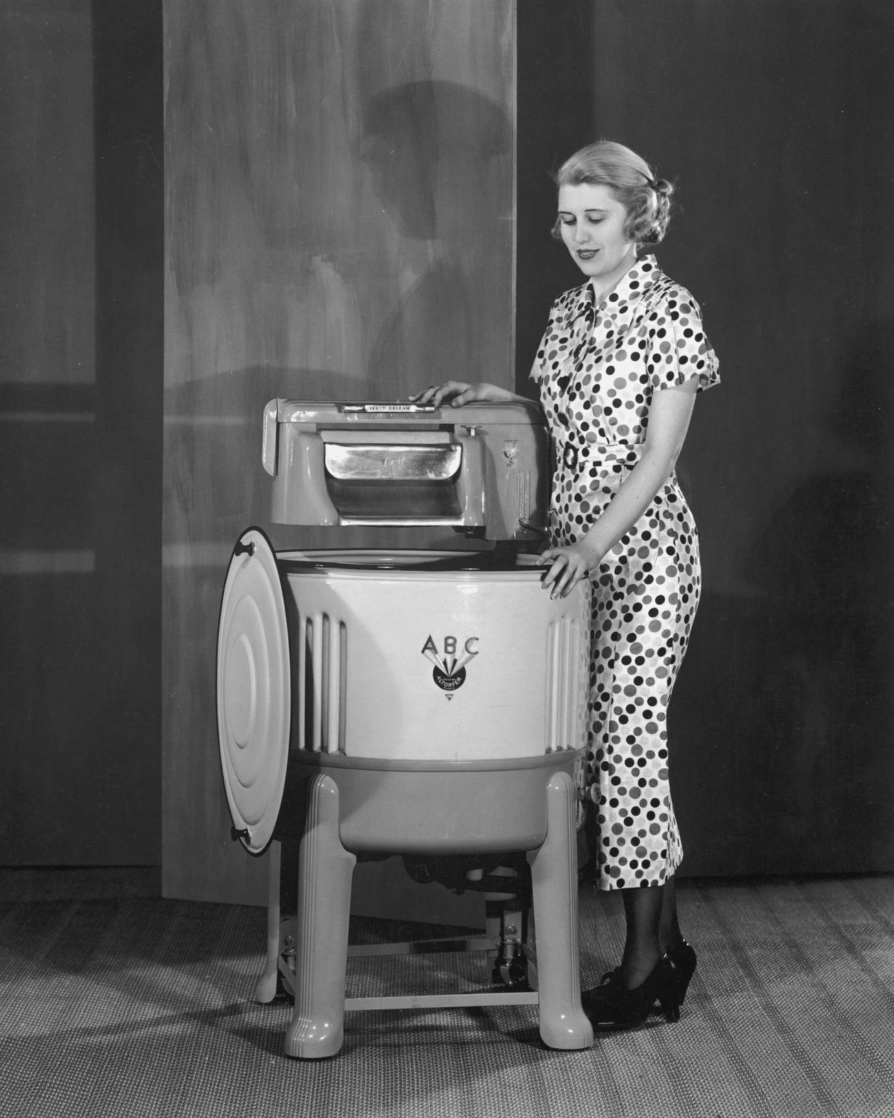 Woman beside a 1930s washing machine with built-in wringer.