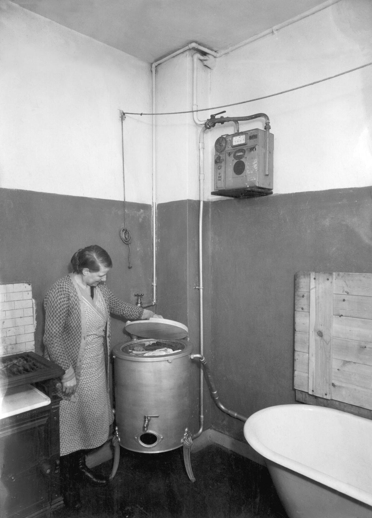 Elderly woman lifting lid of washing machine, UK, 1935.