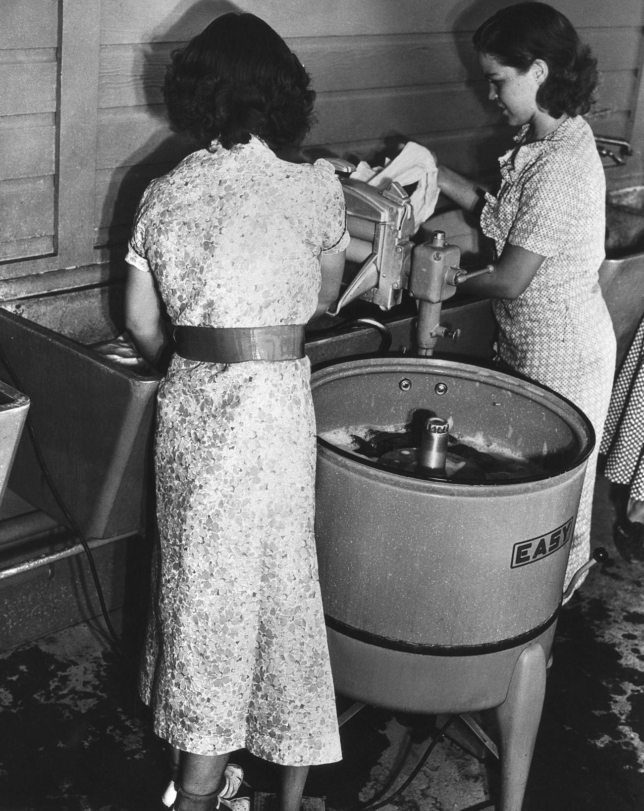 Girls using a wringer at a washing machine.