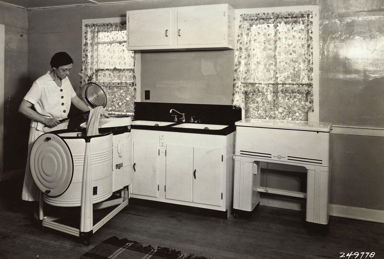 Woman using an early model Westinghouse electric laundry machine.
