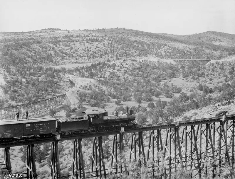 Freight train on a high trestle, two men on car roof, 1895.