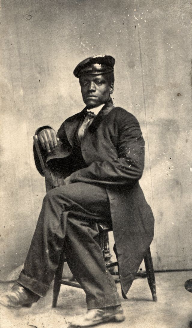 A man sporting a waterproofed cap sits in a chair, one leg over the other. His shoes show evidence of heavy wear