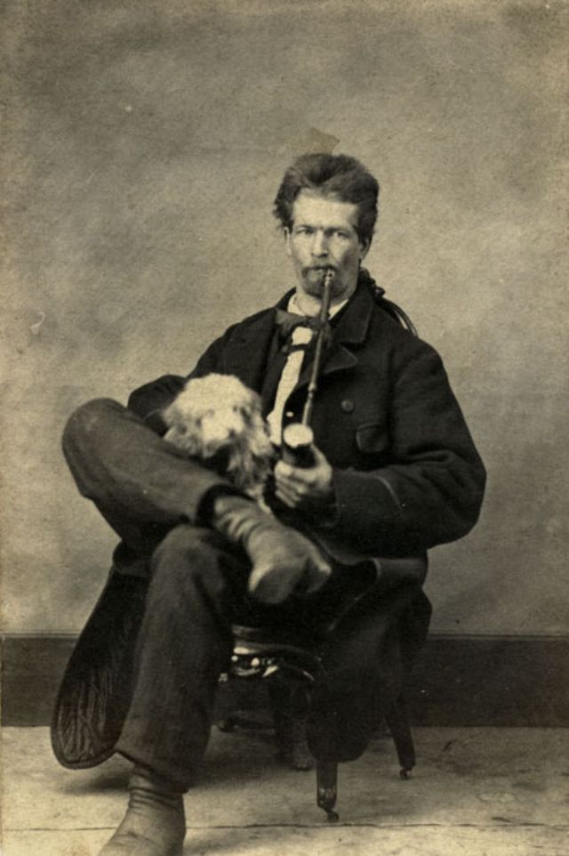 A man with a thick head of hair sits with a puppy and a pipe