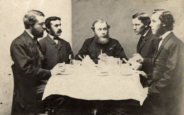 Five men partake of a meal. The presence of bowls and a creamer suggests breakfast
