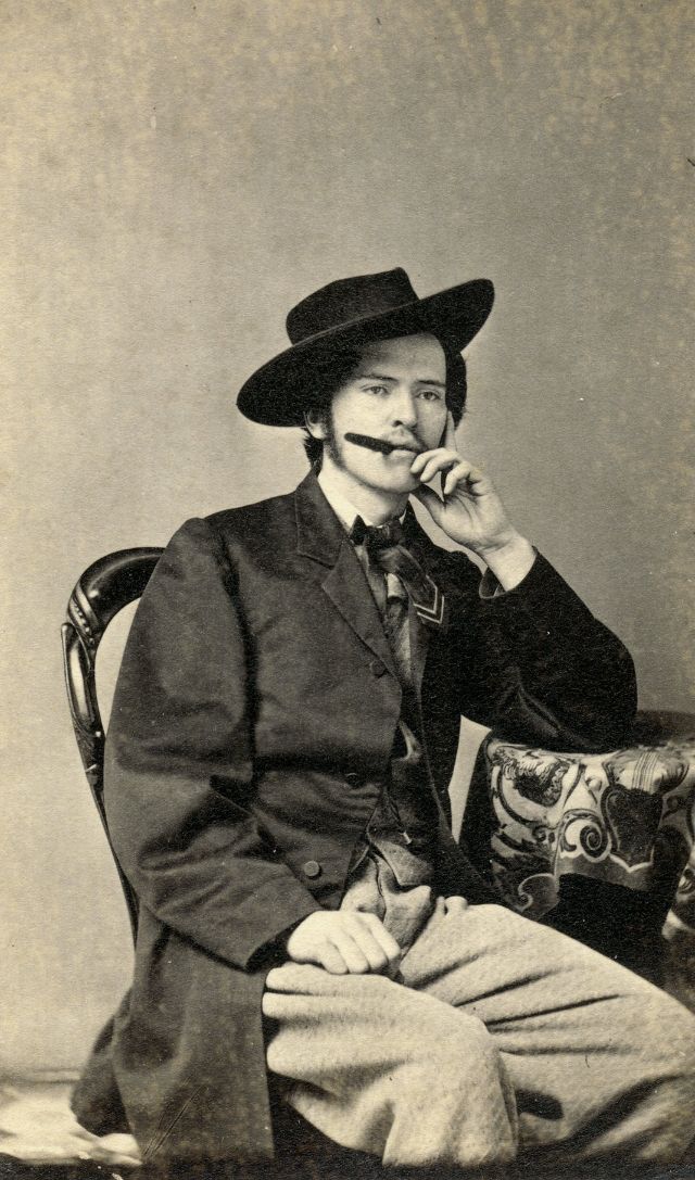 The felt slouch hat, pleated vest and pants, silk tie and tailored frock indicated that this cigar-smoking gent with the light mustache and sideburns is a fashionable Dude of the first order