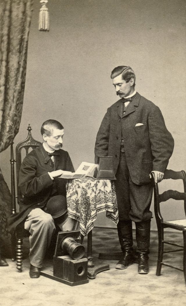 Two gents pose with a wet plate camera equipped with a Petzval lens, a carte de visite album and a stereoviewer
