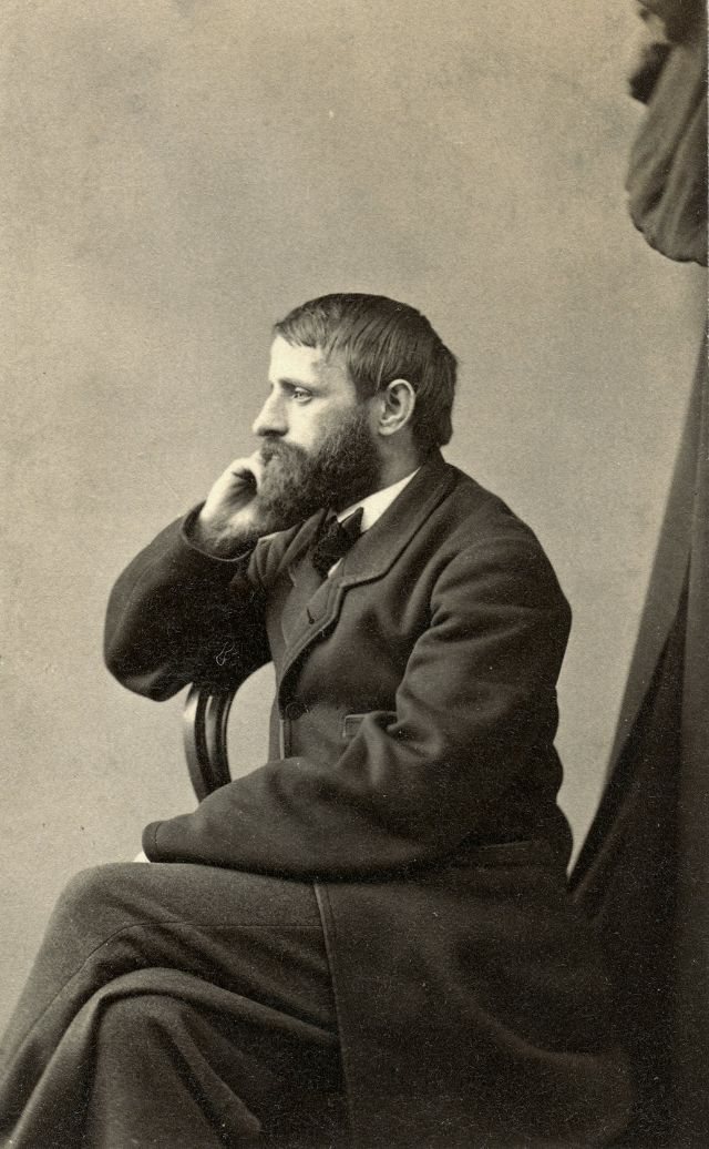 A gentleman sits sideways on a chair, gazing off camera with hand to cheek in what appears to be a contemplative, thoughtful frame of mind