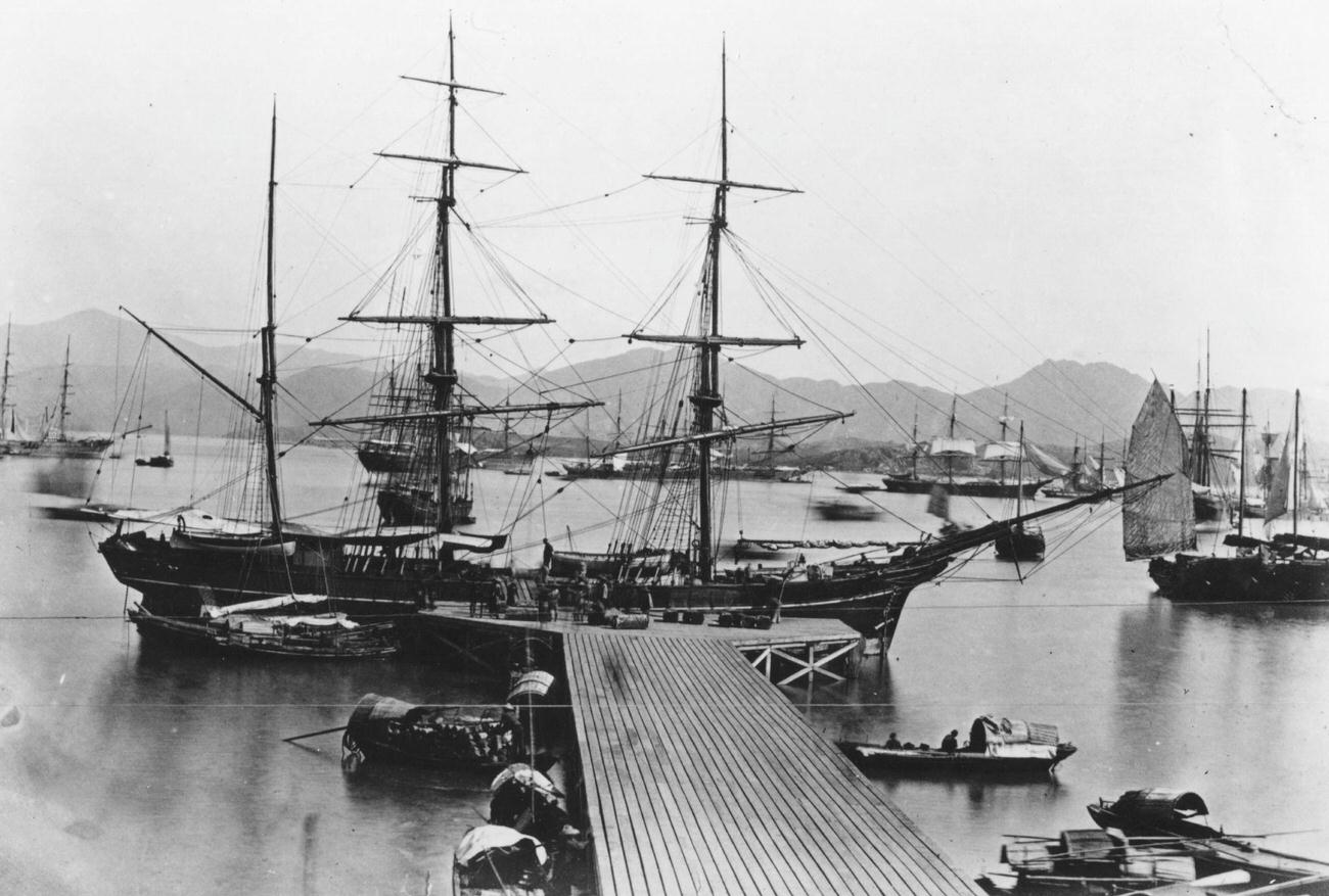 A sailing ship docked at a jetty in Hong Kong harbor, surrounded by other boats, circa 1860.