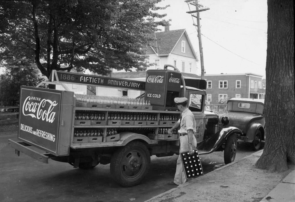 A delivery man unloading cases of Coca-Cola from a truck celebrating the 50th anniversary with a '1886 - Fiftieth Anniversary - 1936' sign.