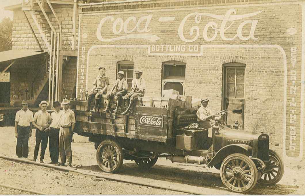 A Coca-Cola delivery truck with three young boys seated on its side, 1900.