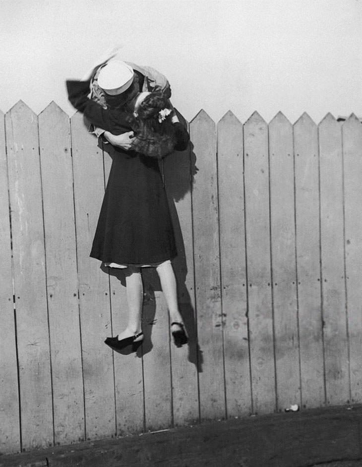 Sailor lifting girlfriend for a kiss over fence, 1945.